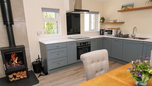 A modern kitchen with grey cabinets, a wood-burning stove, and a dining area with a wooden table and chairs. - Chy-an-oula (Falmouth)
