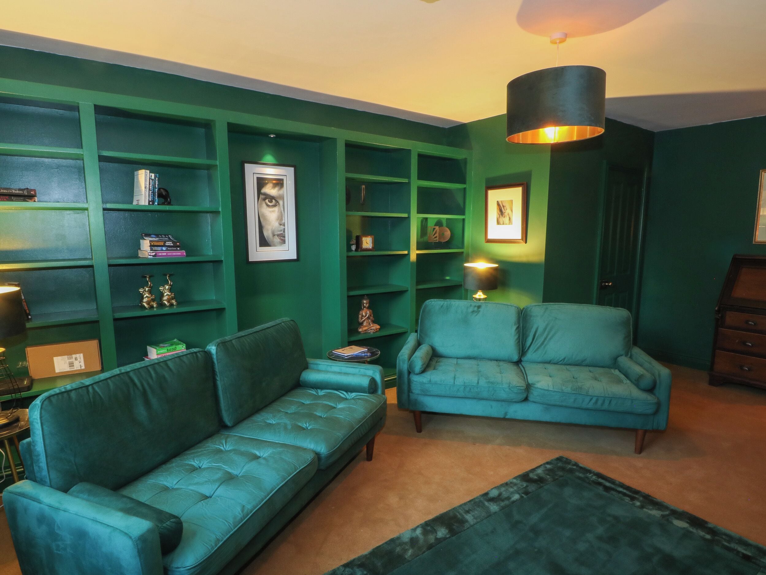 Une pièce avec des canapés de couleur turquoise, des étagères vertes et une lampe suspendue.