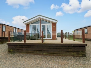 A small wooden building with a glass door and windows, surrounded by a wooden deck and gravel ground.