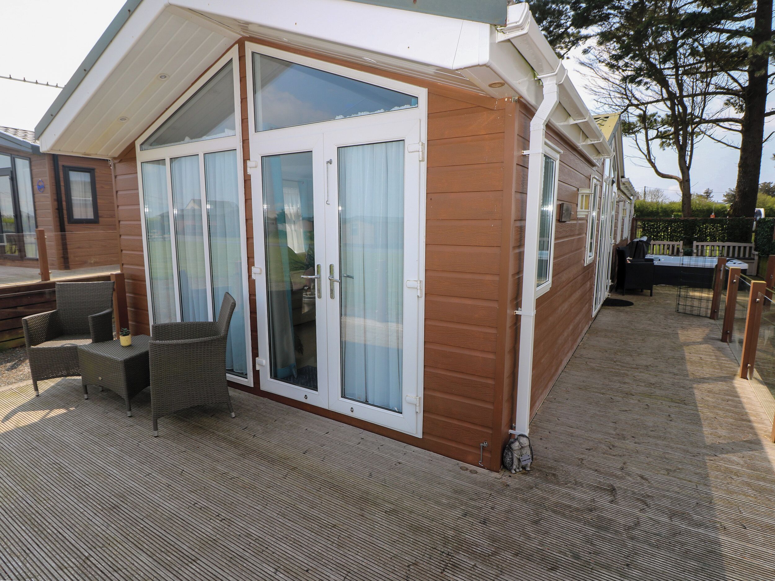 Uma cabana de madeira com porta de correr de vidro, um alpendre com mobiliário de vime e um terraço.
