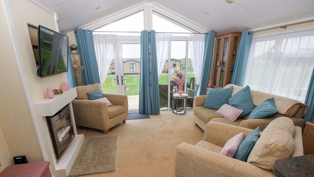 Ein geräumiges Wohnzimmer mit Kamin, zwei Sofas, einem Fernseher und Blick ins Freie.