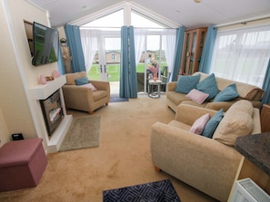 A spacious living room with a fireplace, two sofas, a television, and a view of the outdoors.
