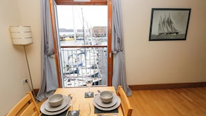 En spiseplads med et bord dækket til to, udsigt over en lysthavn med både, og et indrammet billede af et sejlskib på væggen.