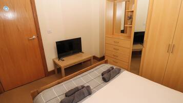 A bedroom with a bed, a TV on a wooden stand, a wardrobe, and a mirror.