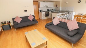 En moderne stue med to grå sofaer, et træbord og et køkken i baggrunden.