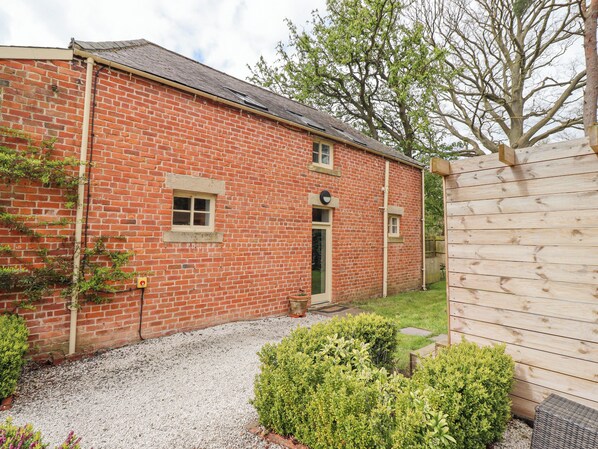 A brick building with a gravel driveway, a wooden fence, and green shrubs. - The Fullerton (Newcastle-upon-Tyne)