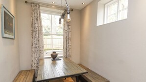 A dining area with a wooden table and bench, a hanging light fixture, and a window with curtains. - The Fullerton (Newcastle-upon-Tyne)
