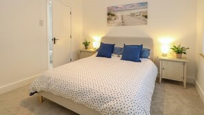 Un dormitorio con una cama, dos mesitas de noche con lámparas, una puerta y un cuadro en la pared.