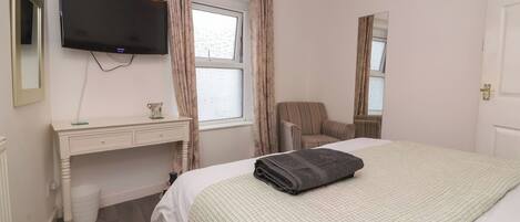 A hotel room with a bed, a desk, a chair, a television, and a window with curtains.