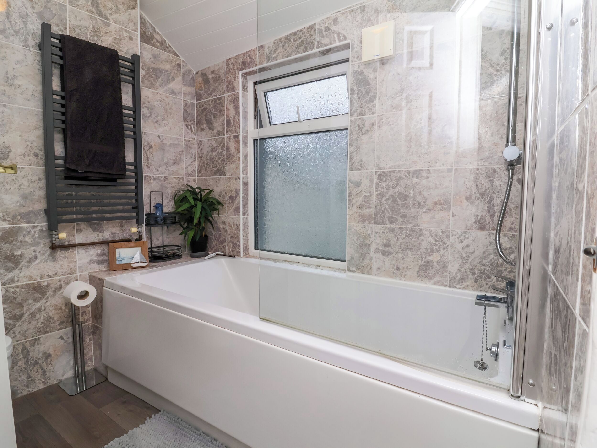 A bathroom with a bathtub, a window, a towel rack, a toilet, and a shower.