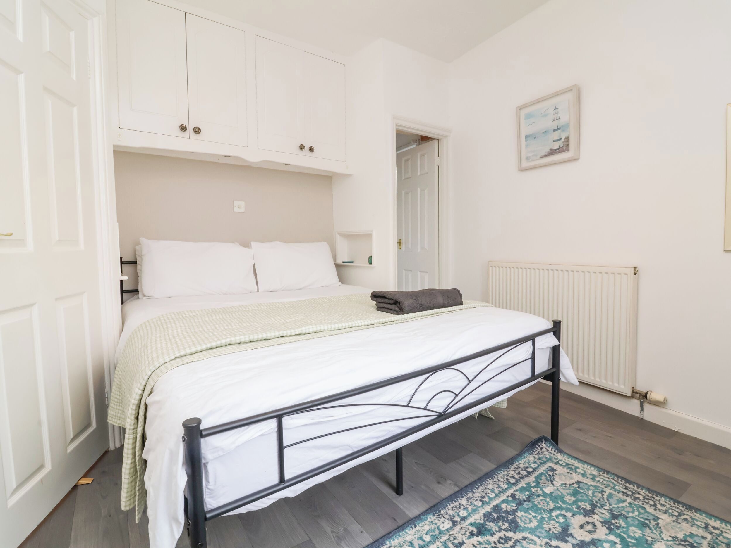 A bedroom with a bed, white walls, a radiator, and a framed picture on the wall.