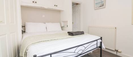 A bedroom with a bed, white walls, a radiator, and a framed picture on the wall.