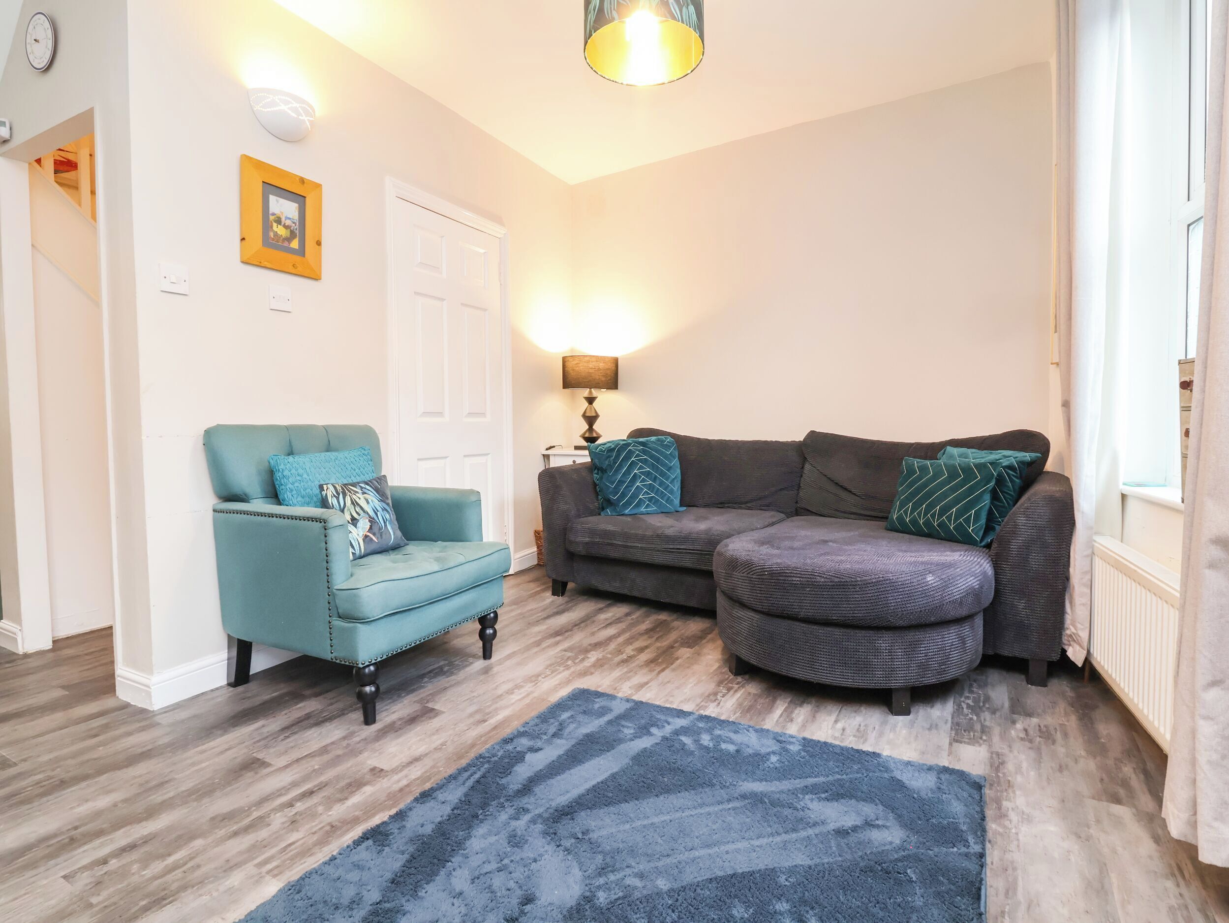 A living room with a teal armchair, a dark grey sofa, and a blue rug.
