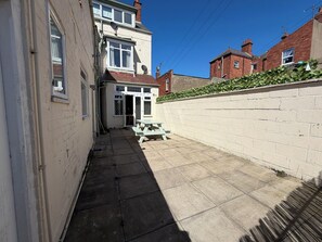 A narrow alleyway with a picnic table, a white door, and a brick wall. - Avalon Lodge (Bridlington)