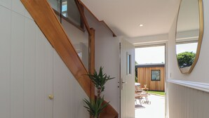 A hallway with a wooden staircase, a potted plant, and a view of an outdoor patio area. - Victory View (Penzance)