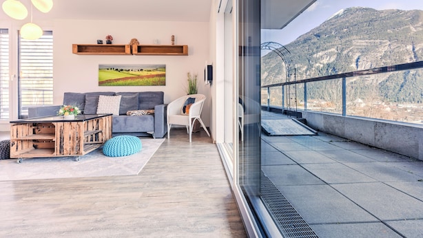 Una sala de estar moderna con un sofá, una mesa de centro de madera y vistas a un paisaje montañoso a través de grandes ventanales.
