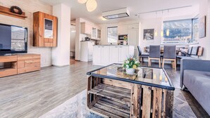 Una cocina moderna con armarios blancos, una mesa de centro de madera y un comedor con sofá y sillas grises.