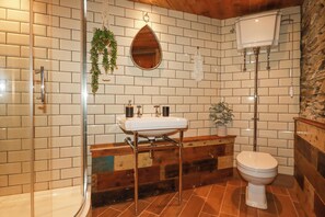 Une salle de bain avec une douche à parois de verre, un lavabo blanc avec un meuble-vasque en bois, des toilettes blanches et une plante suspendue.