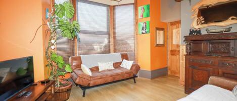 A living room with a brown leather sofa, a television on a wooden stand, a large potted plant, and a wooden cabinet with decorative items.