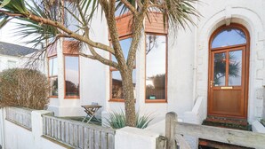 A white building with a wooden door, windows, and a small table outside. - Mermaid's Rest (Newquay)
