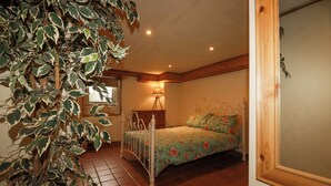 Een slaapkamer met een bed, nachtkastje, lamp en een grote potplant.
