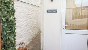 Een witte deur met een bord waarop 'The Cave' staat en een raam met zonwering.