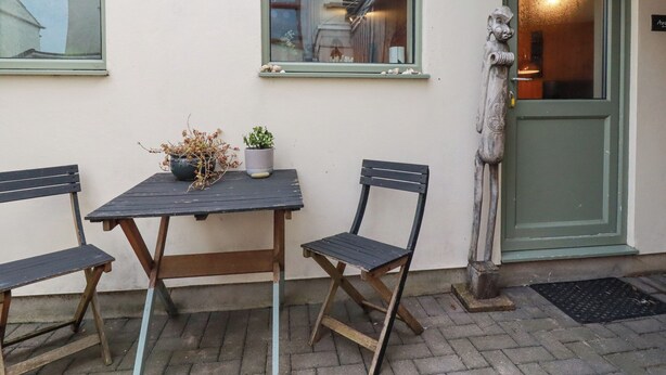 An outdoor seating area with a table and two chairs, a potted plant, and a statue on the wall. - The Aqua Shack (Newquay)