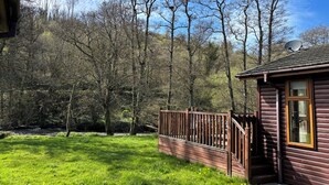 A cabin with a wooden deck, a satellite dish, and a view of a forested area.