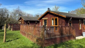 A wooden cabin with a fenced deck, large windows, and a satellite dish.