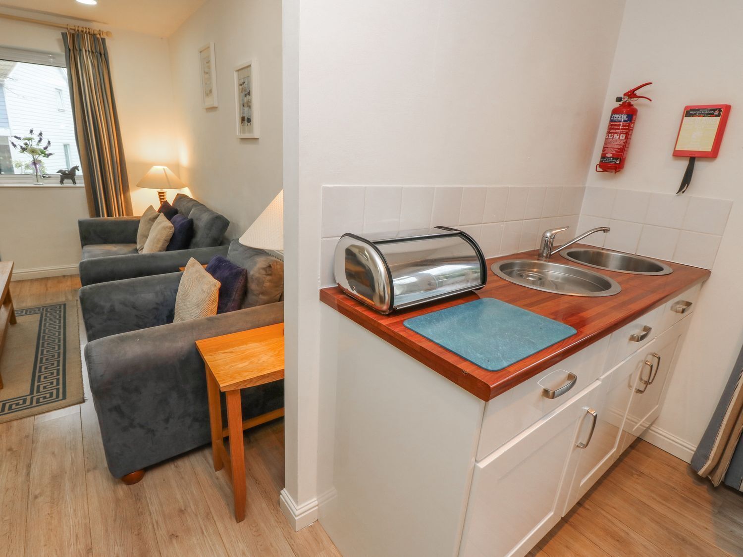 A compact living space with a kitchenette, a sofa set, a small dining table, and a window with curtains.