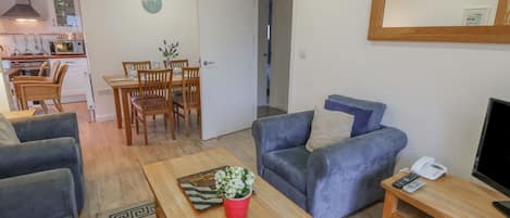 A modern living room with a sofa, a coffee table with a plant, and a TV stand with a phone and remote controls.