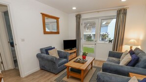 A living room with two grey sofas, a wooden coffee table, a TV on a stand, and a mirror on the wall. - Pierpont D1 (Yarmouth)