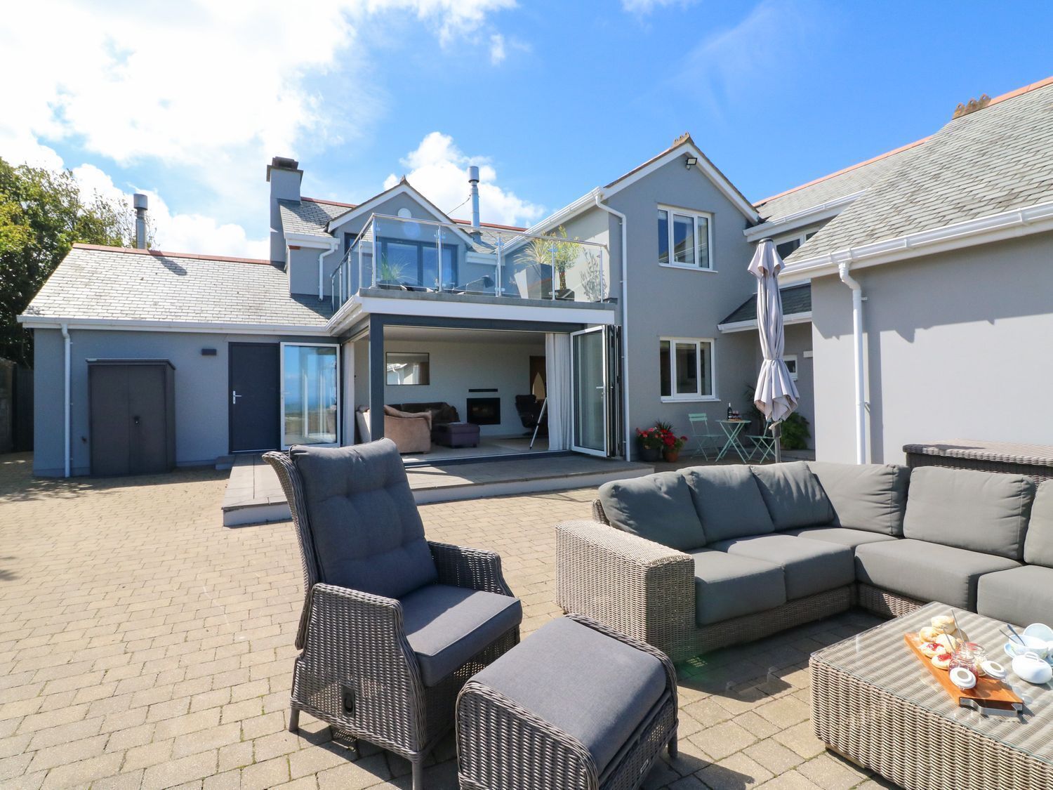 A modern house with a patio area featuring wicker furniture and a dining table with food.