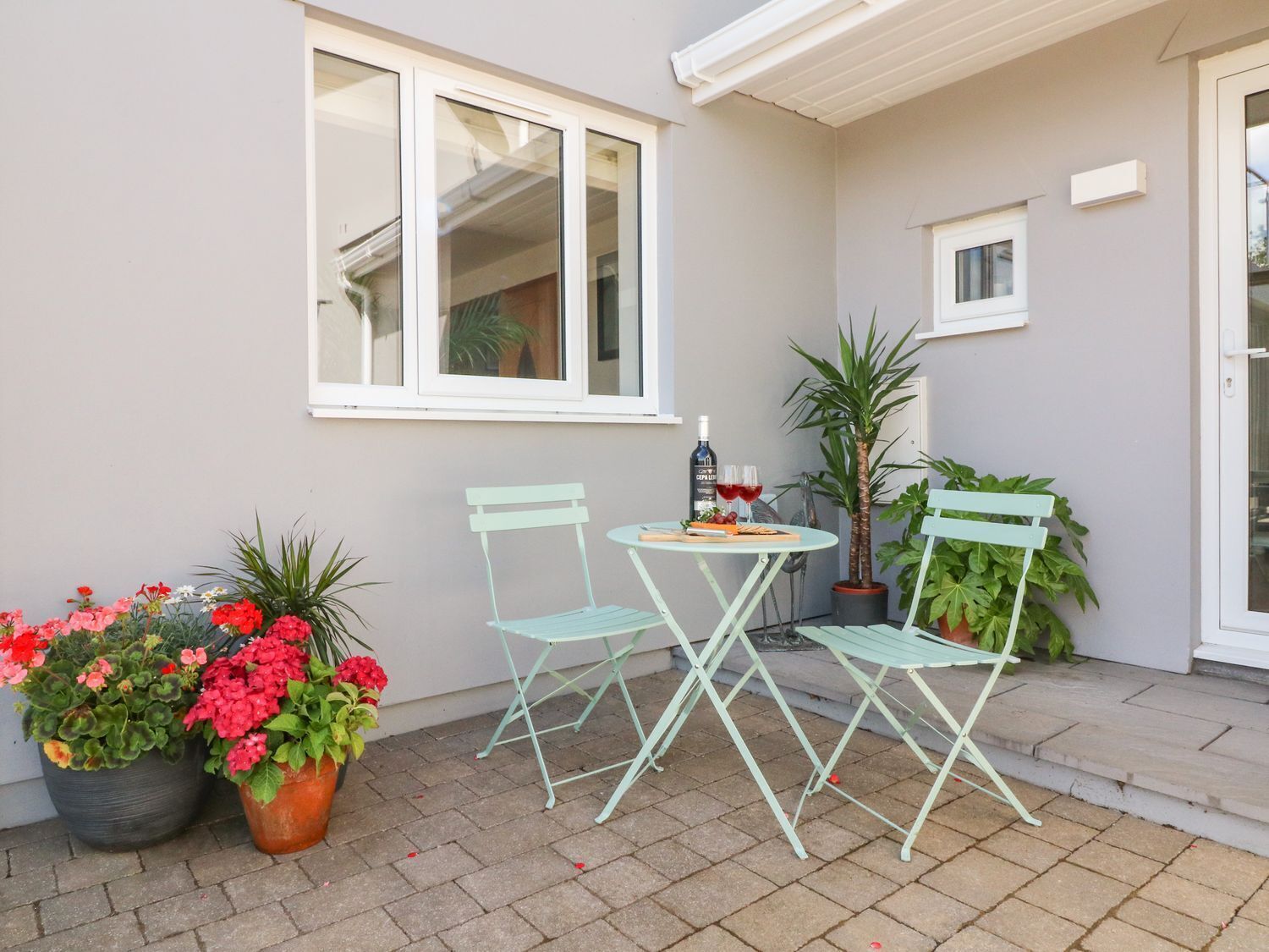 A patio with two light blue chairs, a small round table, and potted plants.