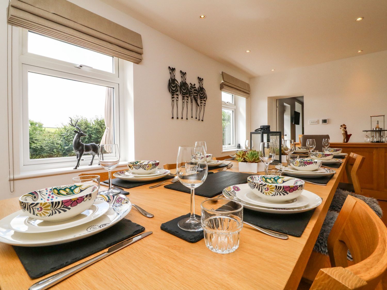 A dining area with a long table set for a meal, decorated with patterned bowls and wine glasses.