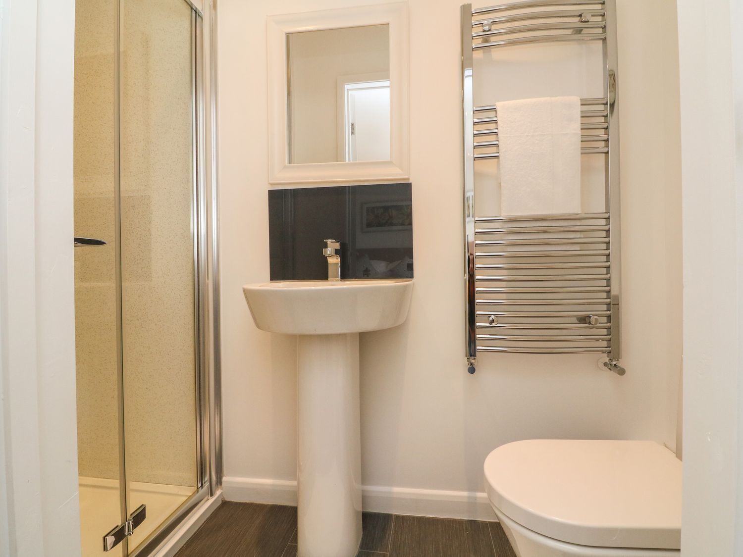 A bathroom with a glass shower enclosure, a pedestal sink, a toilet, and a towel rack.