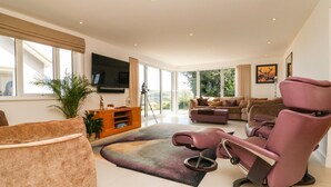 Een ruime woonkamer met een groot raam, een flatscreentelevisie, een bank, een fauteuil en een houten tv-meubel.