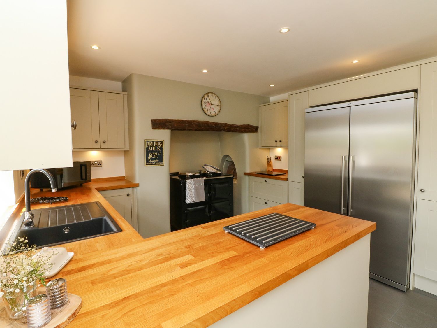 A modern kitchen with a wooden countertop, stainless steel appliances, and a clock on the wall.