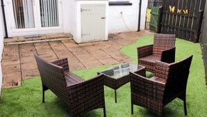 A patio with wicker furniture and a glass table, surrounded by artificial grass and a brick floor. - Portstewarts Home From Home (Portstewart)