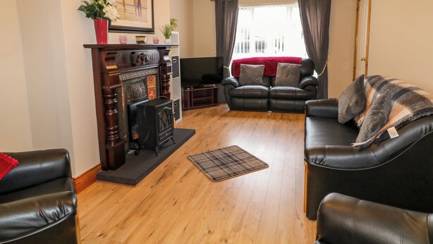 A living room with a fireplace, leather sofas, a television, and a large window with curtains. - Portstewarts Home From Home (Portstewart)
