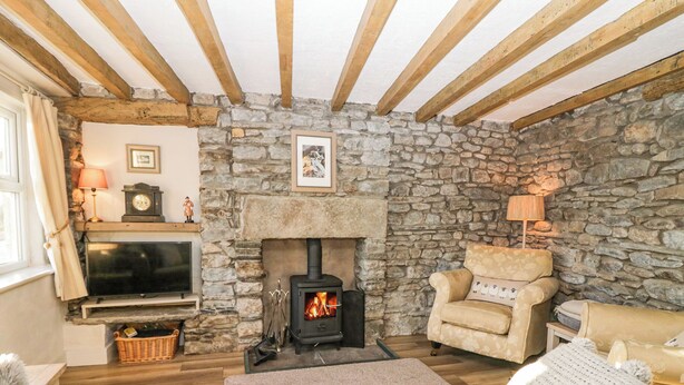 A cozy living room with a stone wall, wooden beams, a fireplace, a television, and comfortable seating. - Holme Fell View (Sedbergh)
