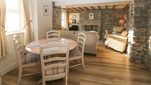 A cozy room with a stone fireplace, wooden beams, a dining table with chairs, and a sofa. - Holme Fell View (Sedbergh)