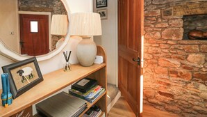 A cozy entryway with a wooden door, a stone wall, a mirror, a lamp, and a framed picture on a shelf. - Holme Fell View (Sedbergh)