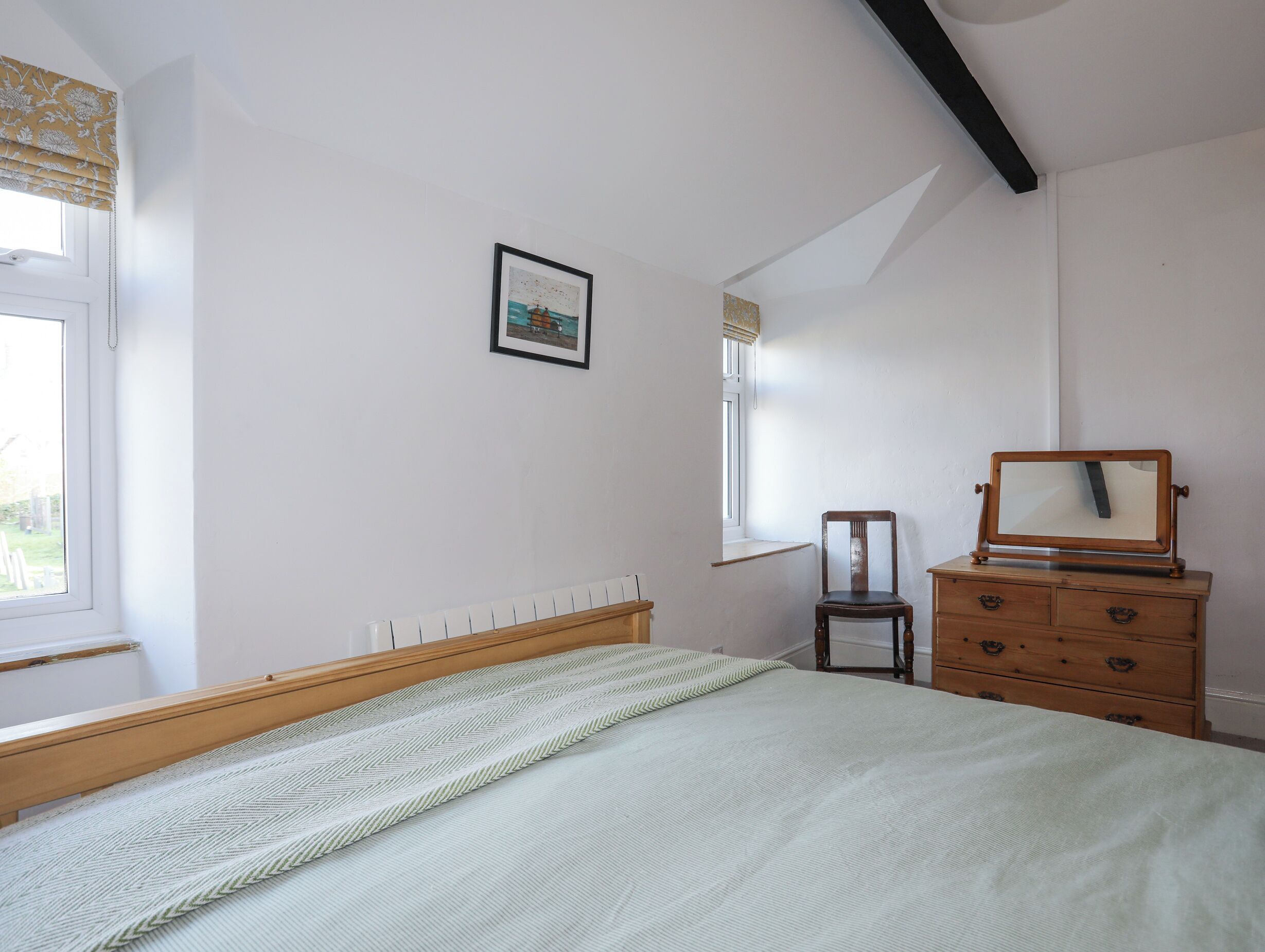 Un dormitorio con cama, cómoda, silla, ventana y un cuadro en la pared.