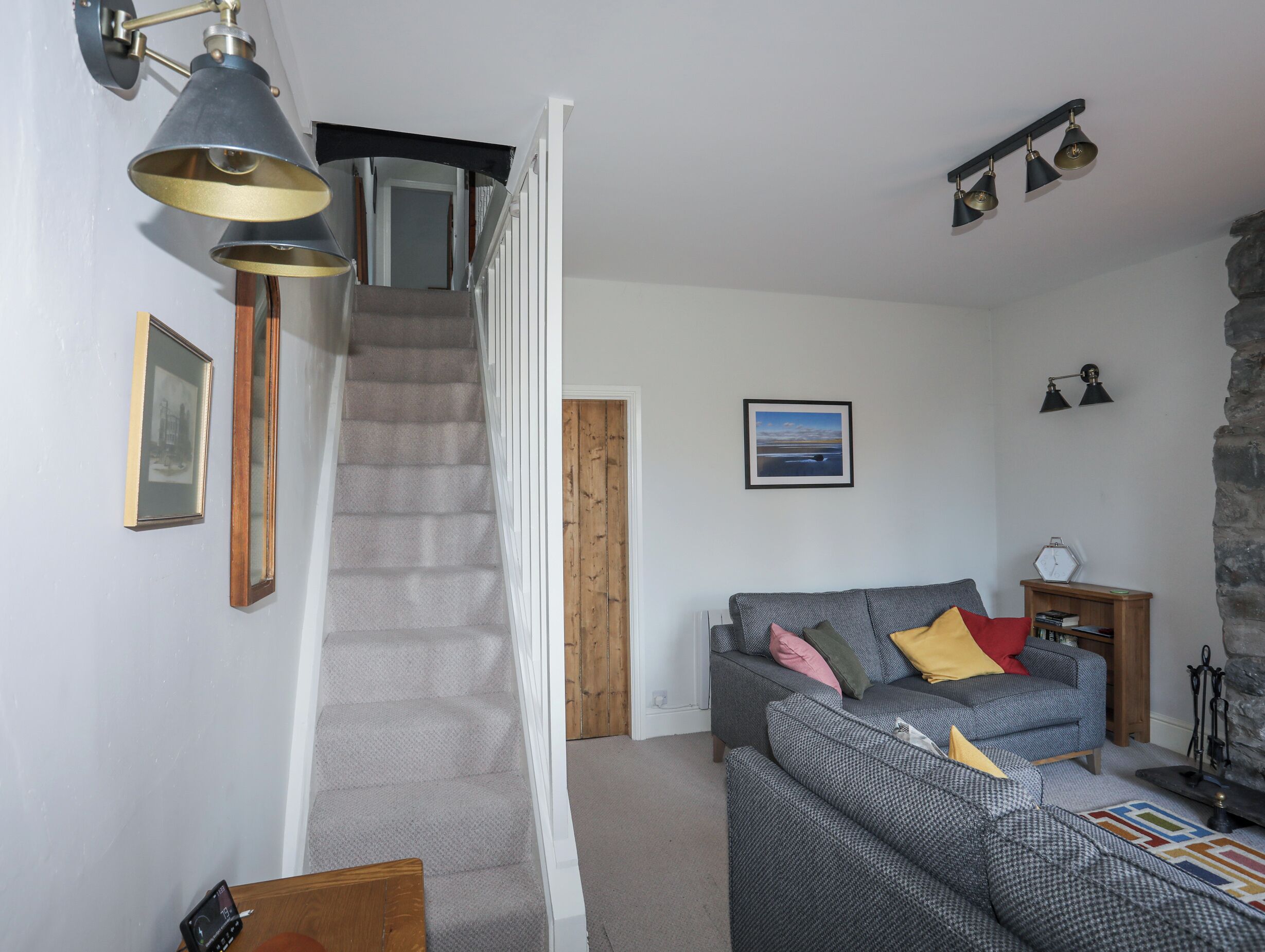 Un escalier menant à un palier, un canapé gris avec des coussins, une porte en bois et un tableau encadré au mur.