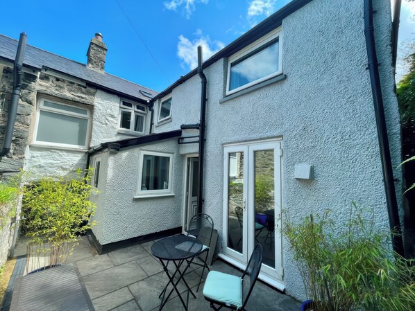 A two-story house with a stone facade, a tiled patio, and a glass door leading to a covered outdoor area. - Gwelfor (Harlech)
