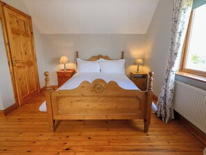 A wooden bed in a room with a wooden floor, two bedside tables with lamps, a wooden wardrobe, and a window with curtains.