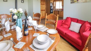 Un coin repas avec une table en bois dressée pour quatre personnes, un canapé rouge et une cuisine en arrière-plan.