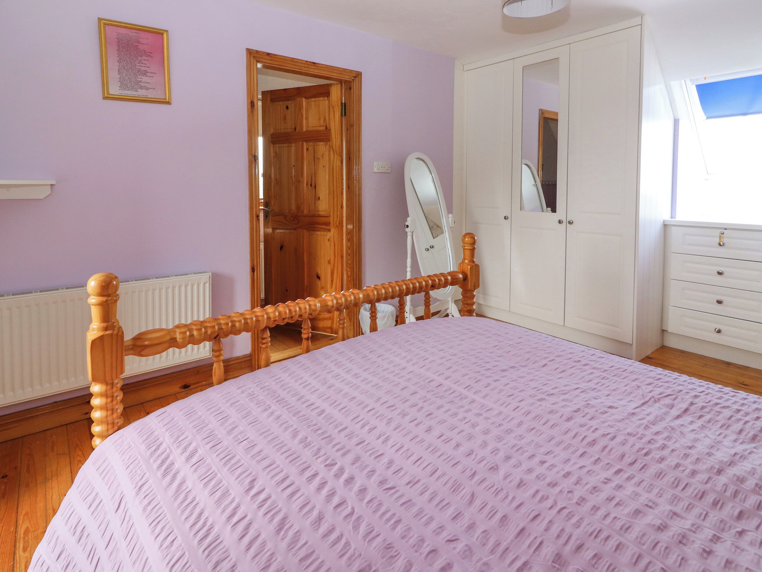 A bedroom with a wooden bed frame, a white dresser, a mirror, and a door leading to another room.