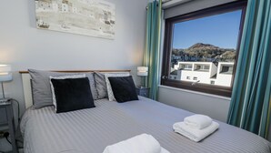 A hotel room with a bed, two pillows, a nightstand with a lamp, a window with curtains, and a painting on the wall. - Estuary Escape (Porthmadog)